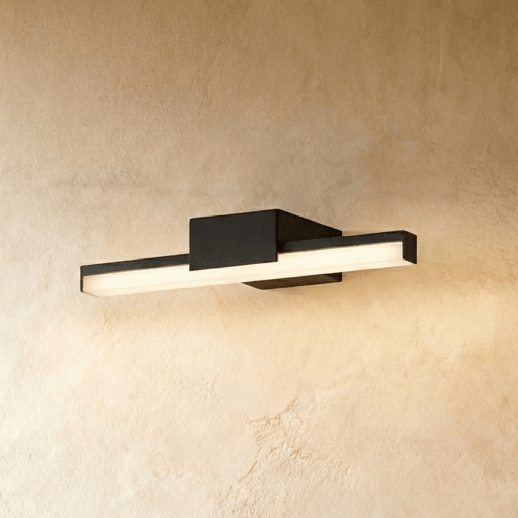 Clérachic slim black linear wall light with a square backplate, glowing warm against a textured limewash wall.