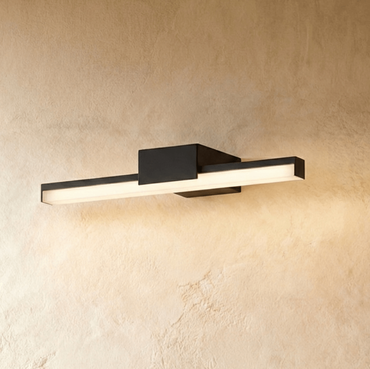 Clérachic mid-length black linear wall light with frosted diffuser and square mount, lit warm on a limewash wall.