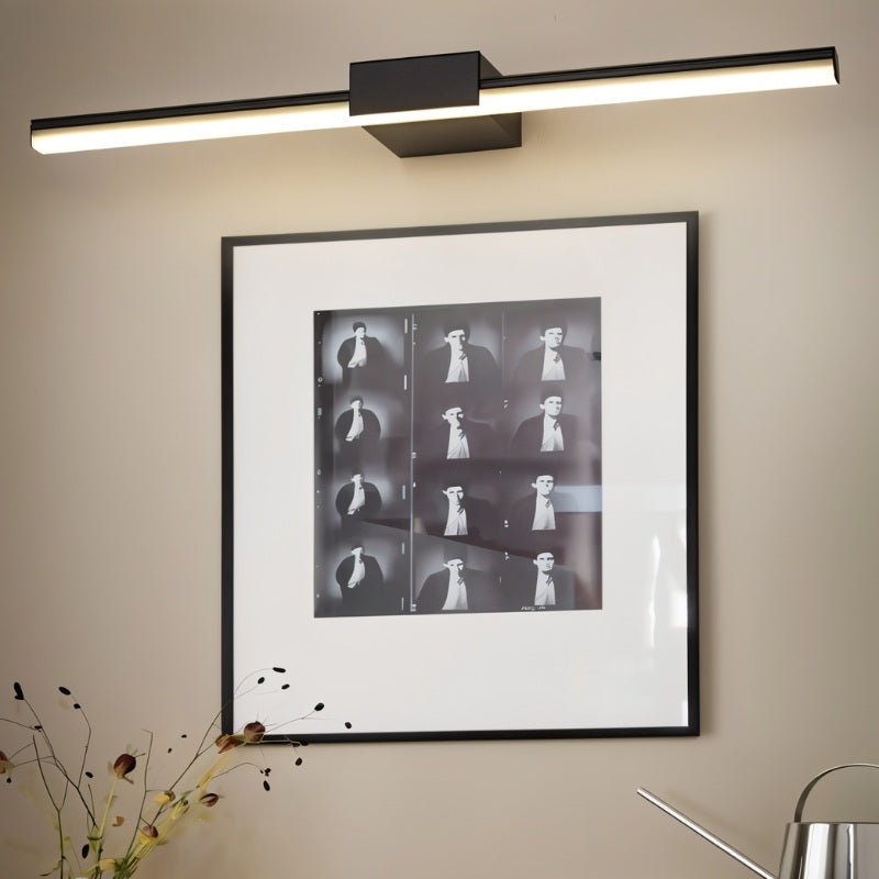Clérachic black linear wall light above a framed black-and-white photographic print, beside dried stems and a steel can.