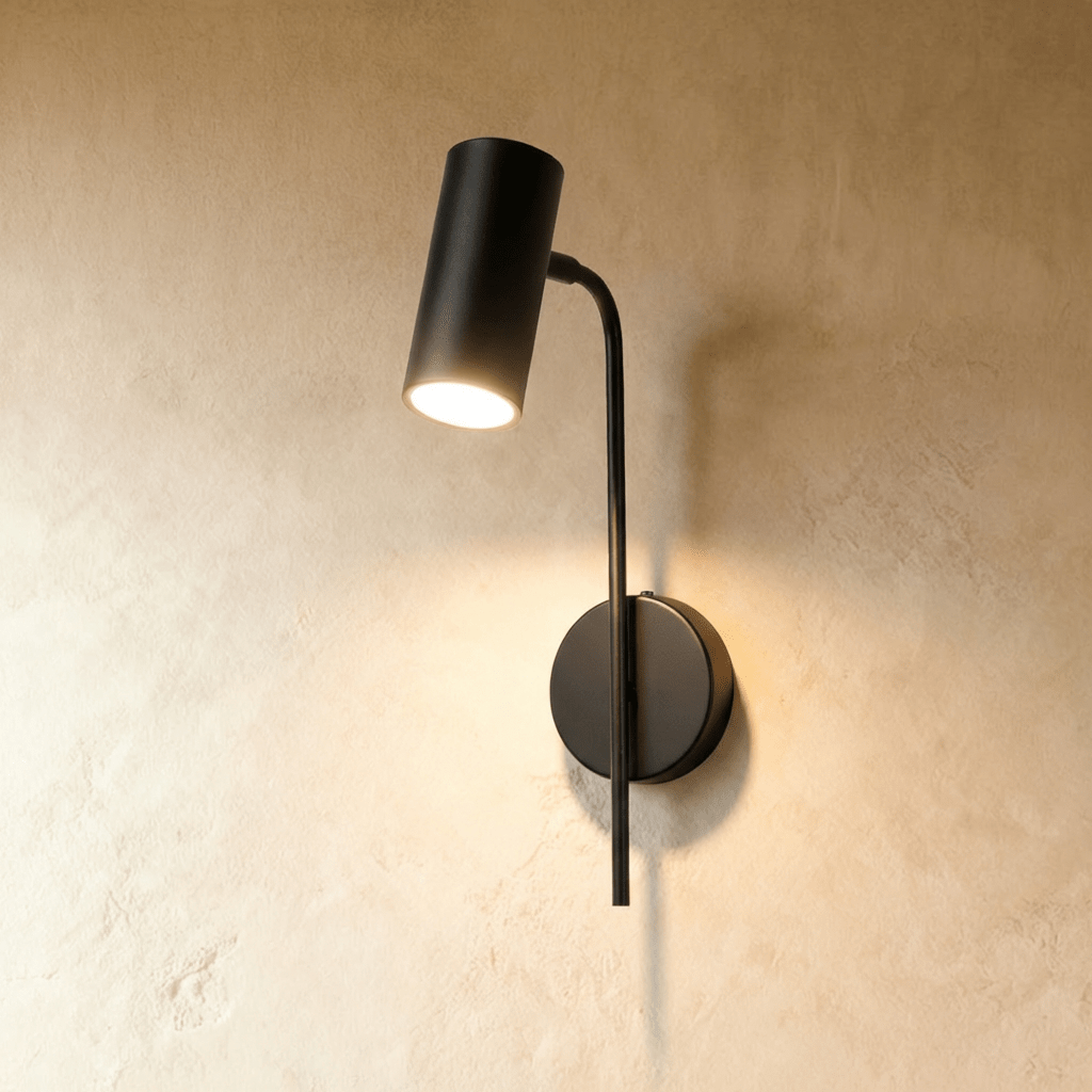 Clérachic black wall reading light with a cylinder spot on a slim curved arm and round plate, glowing on plaster.