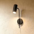 Clérachic black wall reading light with a cylinder spot on a slim curved arm and round plate, glowing on plaster.