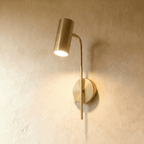 Clérachic brushed gold wall reading light, a cylinder spot on a slim curved arm, lit warm against limewash.