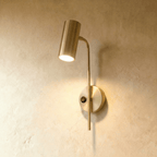 Clérachic brushed gold wall reading light with a small black rocker switch on its round plate, lit warm.