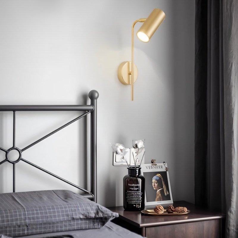 Clérachic gold wall reading light above a bedside table with a dark vase, framed print and a metal bed frame.