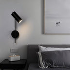 Clérachic black wall reading light angled down beside a grey headboard, above a black bedside table.