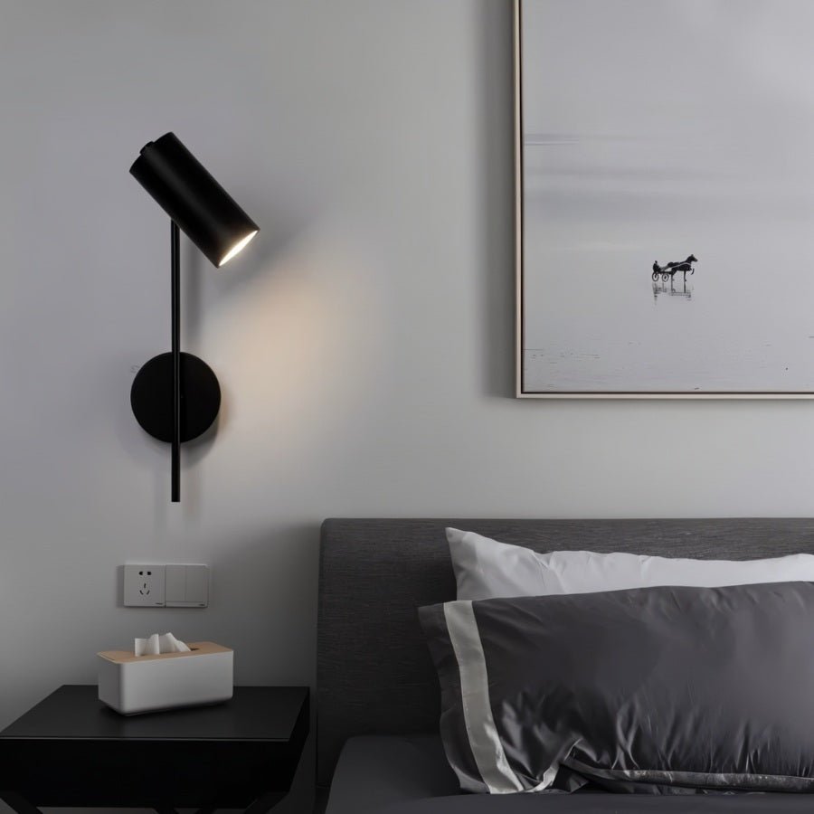 Clérachic black wall reading light angled down beside a grey headboard, above a black bedside table.