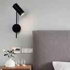 Clérachic black wall reading light angled to a pillow, beside a textured grey headboard and a small white vase.