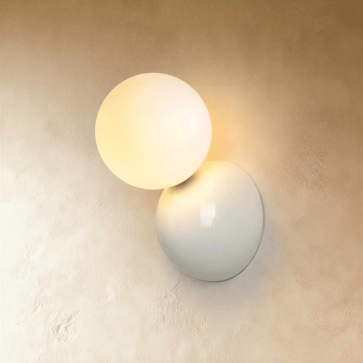 Clérachic white wall lamp with a frosted glass globe lit warm beside a glossy round disc plate, on a plaster wall.