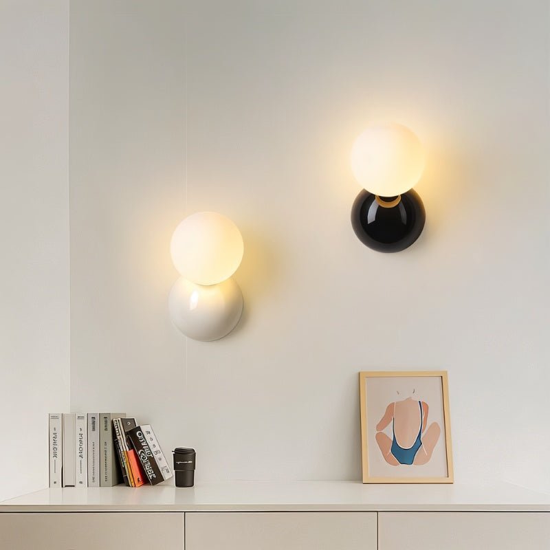 Clérachic white and black wall lamps with lit globes above a shelf of books, a small framed print and a coffee cup.