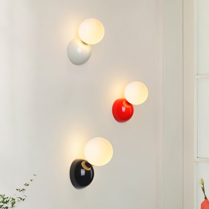 Clérachic white, red and black wall lamps with lit frosted globes stepped down a pale wall in a bright room.
