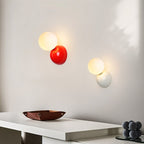 Clérachic red and white wall lamps with lit frosted globes on a pale wall above a white console and a leather tray.