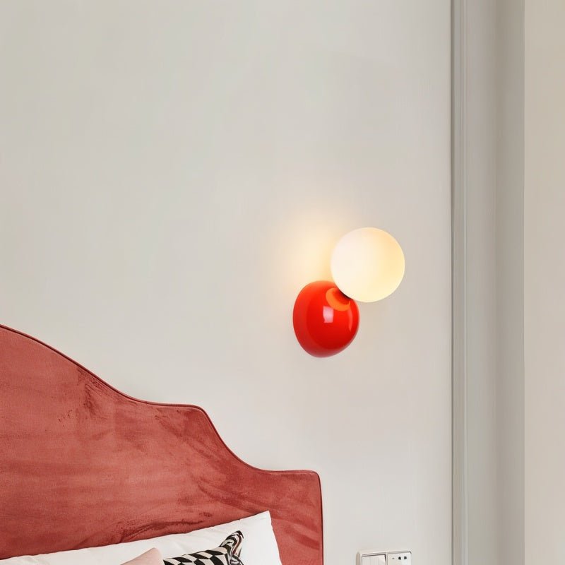 Clérachic red wall lamp with a lit frosted globe on a pale wall beside a rose-pink velvet headboard.