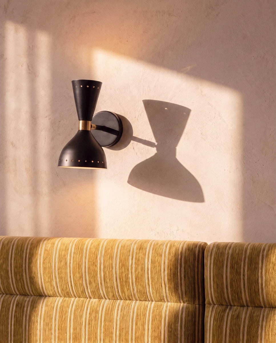 Clérachic wall lamp in matte black casting a dramatic hourglass shadow across a sunlit plaster wall.