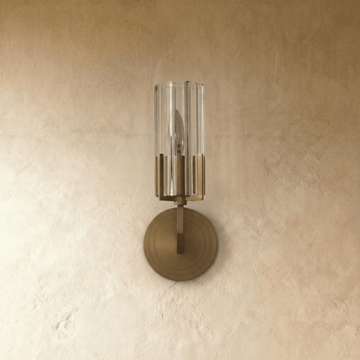 Clérachic brass wall light switched off, showing the ribbed clear glass shade, candle-style bulb and stepped round backplate.
