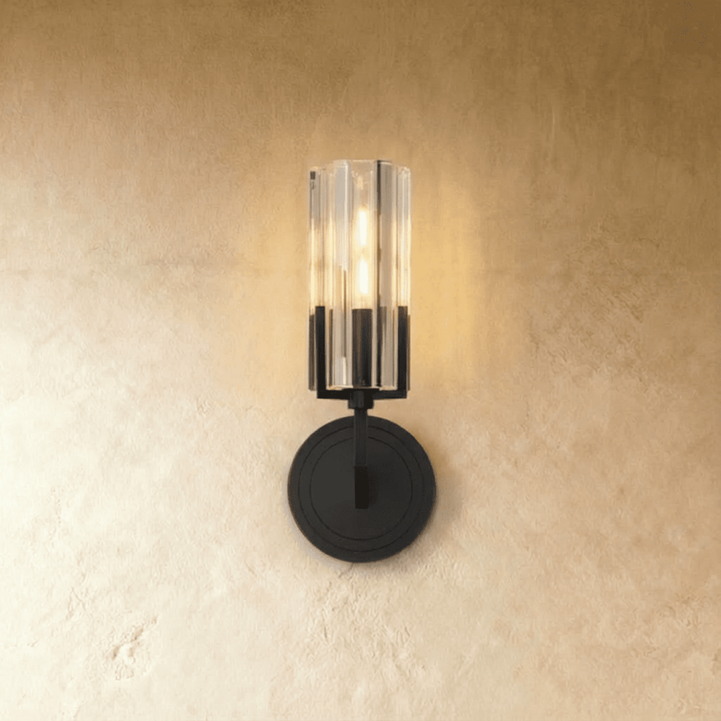 Clérachic black wall light with a fluted glass cylinder shade lit warmly, mounted on a round stepped backplate against plaster.