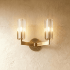 Clérachic twin-arm brass wall light with two fluted glass shades lit warmly, mounted on a limewashed wall.