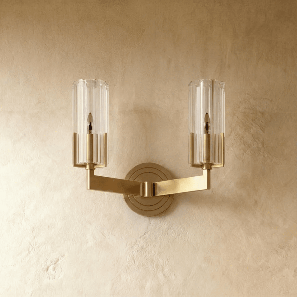 Clérachic twin-arm brass wall light unlit, showing two ribbed glass cylinders on angular arms and a stepped round backplate.