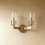 Clérachic twin-arm brass wall light unlit, showing two ribbed glass cylinders on angular arms and a stepped round backplate.