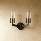 Clérachic twin-arm black wall light switched off, with two ribbed glass cylinders and a matching round backplate on plaster.