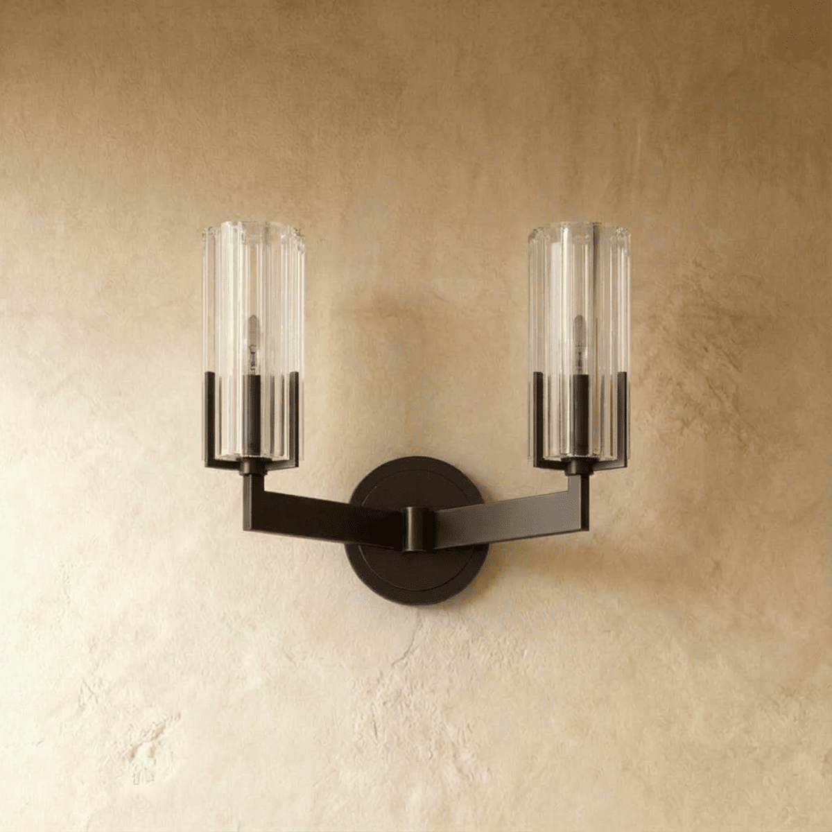 Clérachic twin-arm black wall light switched off, with two ribbed glass cylinders and a matching round backplate on plaster.
