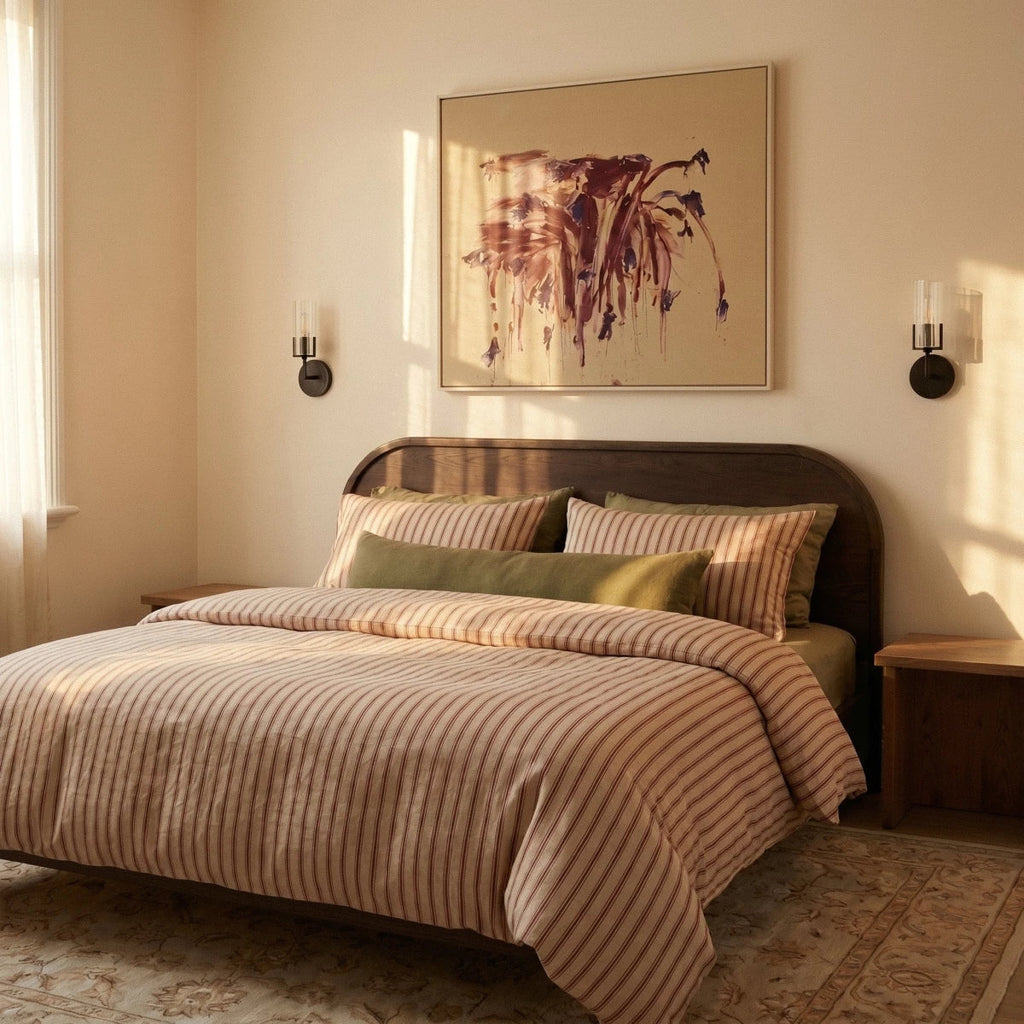 Pair of Clérachic black wall lights flanking an abstract painting above a bed with striped linen, in warm evening light.