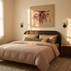 Pair of Clérachic black wall lights flanking an abstract painting above a bed with striped linen, in warm evening light.