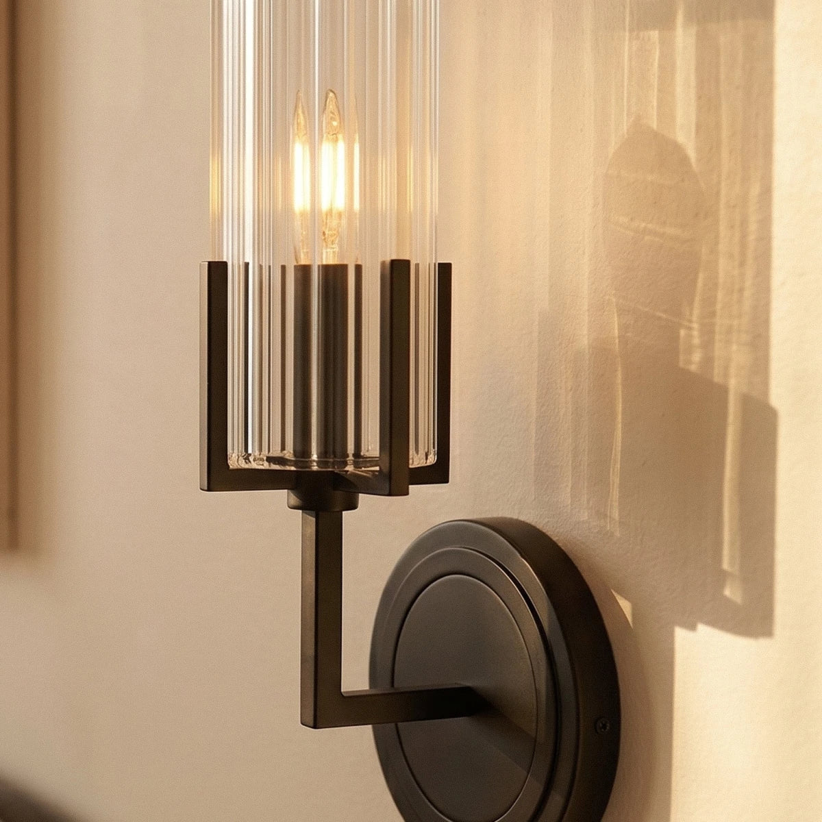 Close crop of the Clérachic black wall light, with two candle bulbs lit in a ribbed glass shade and a square-section metal arm.
