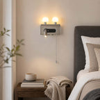 A nickel Clérachic wall light lights the wall beside a bed with a grey headboard, its two globes and spotlight switched on.