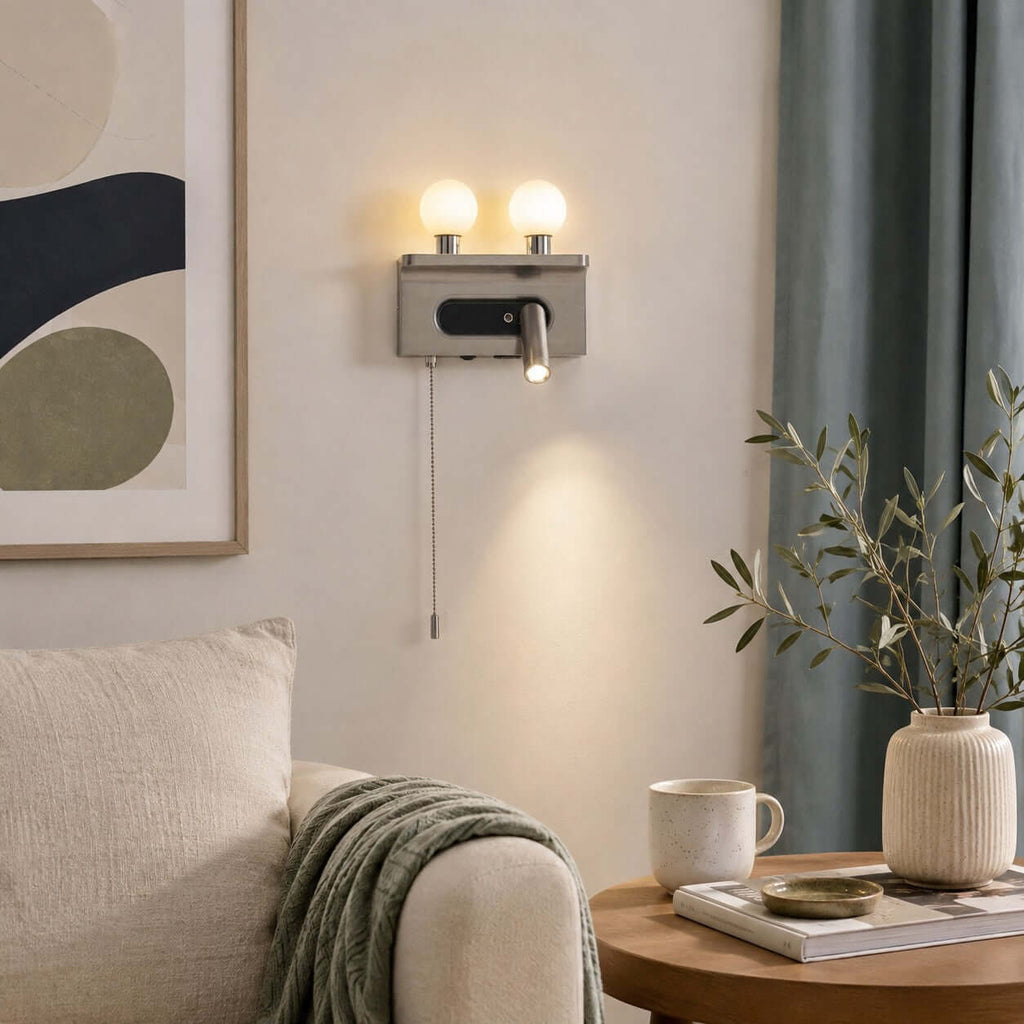 This Clérachic wall light, finished in nickel, casts a pool of light from its spotlight above a sofa arm and a round side table.