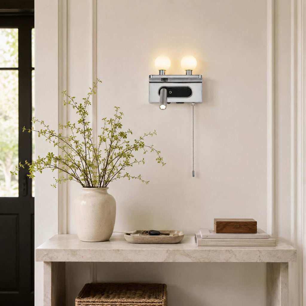 Chrome Clérachic wall light with two globes and a spotlight, hung over a pale stone console in a panelled hallway.