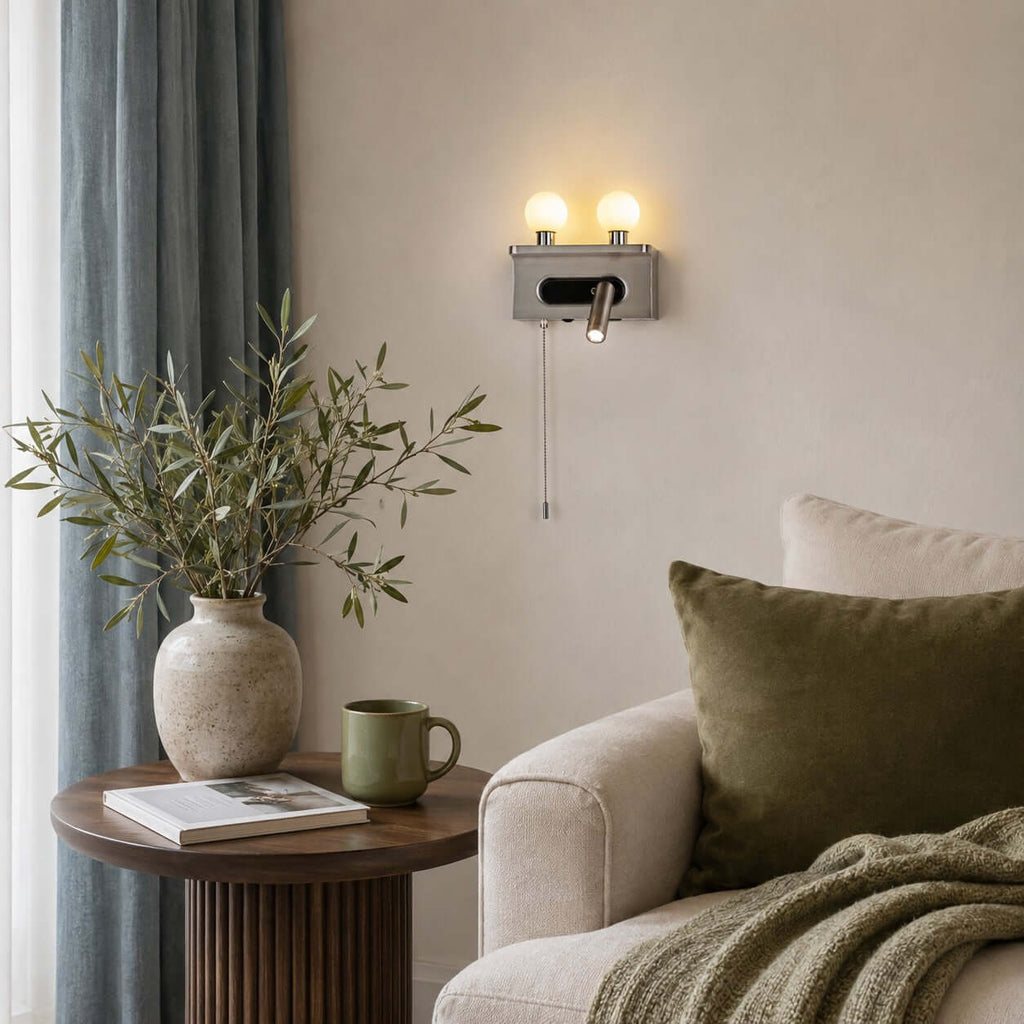 A nickel Clérachic wall light hangs above a round fluted side table and an armchair with an olive cushion beside blue curtains.