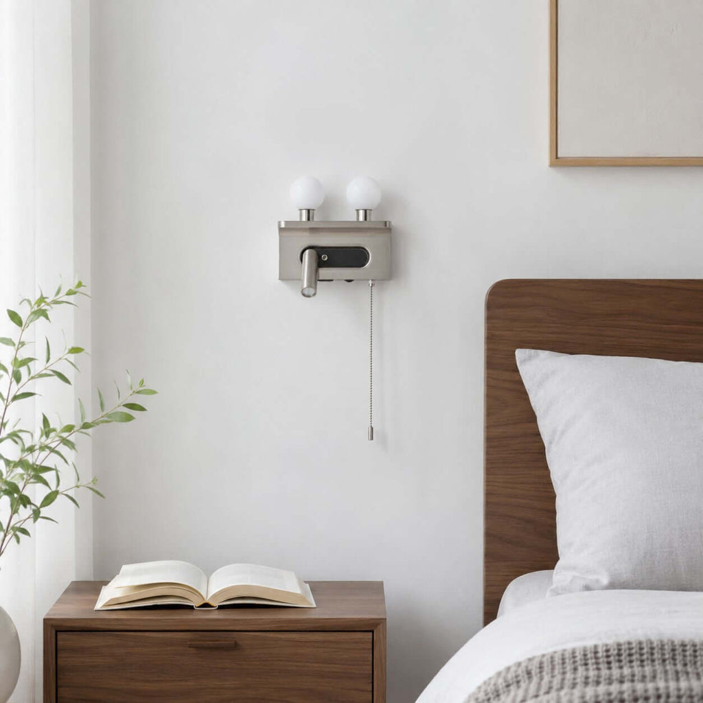The nickel Clérachic wall light, switched off, sits on a white wall above a walnut bedside table with an open book.