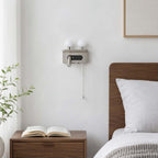 The nickel Clérachic wall light, switched off, sits on a white wall above a walnut bedside table with an open book.