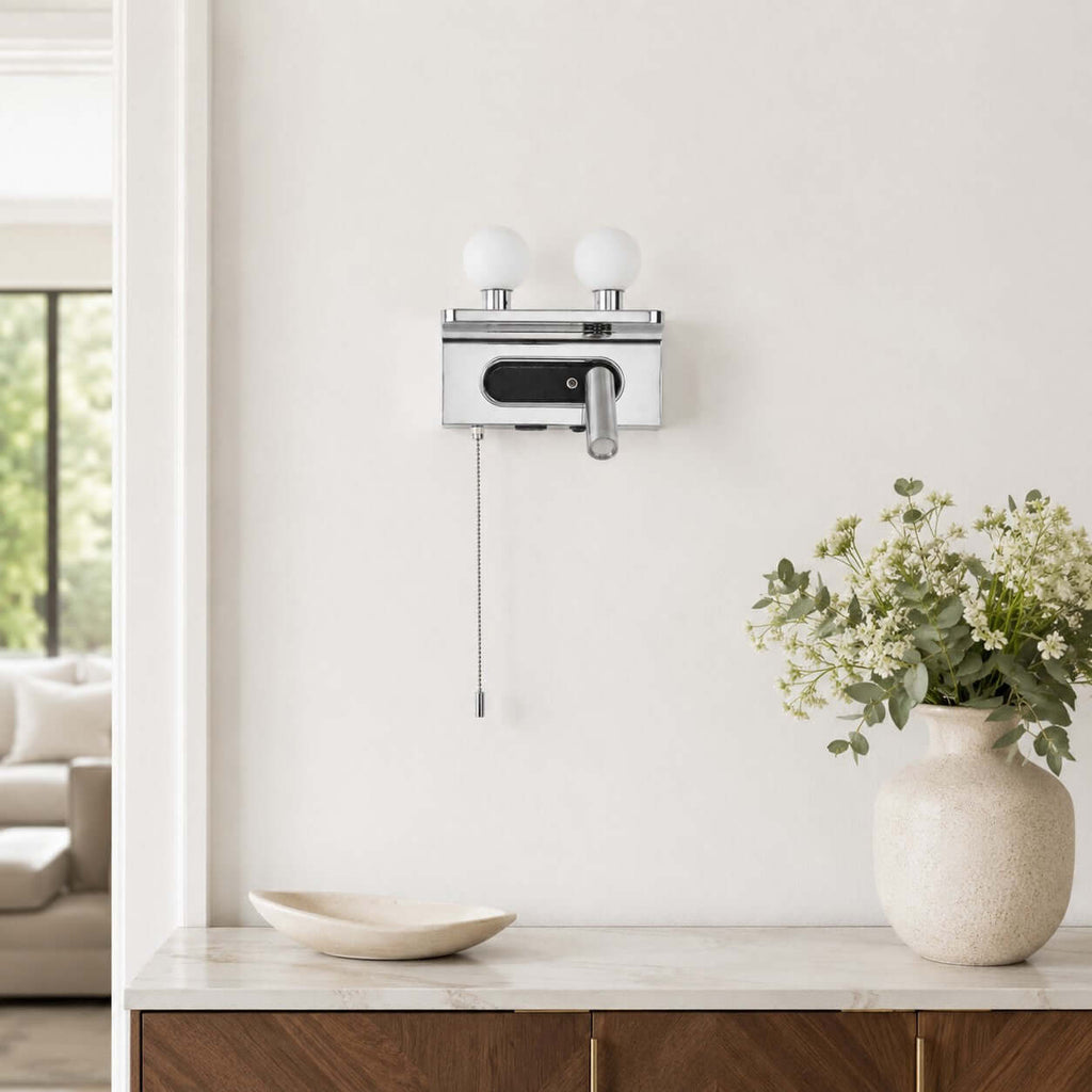 A chrome Clérachic wall light with unlit white globes hangs above a marble-topped sideboard with a vase of flowers.
