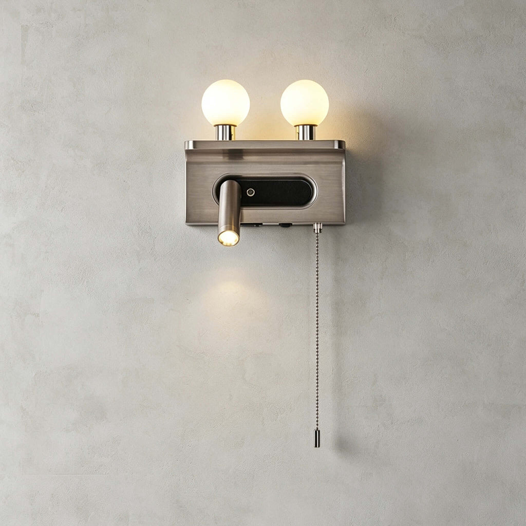 Nickel Clérachic wall light with two lit globes and a small spotlight with a pull chain, shown on a plain grey wall.