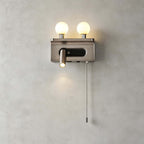 Nickel Clérachic wall light with two lit globes and a small spotlight with a pull chain, shown on a plain grey wall.