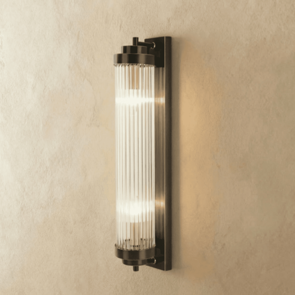 Clérachic wall light in dark bronze-black with a ribbed glass rod cylinder and two lit bulbs, on limewash.