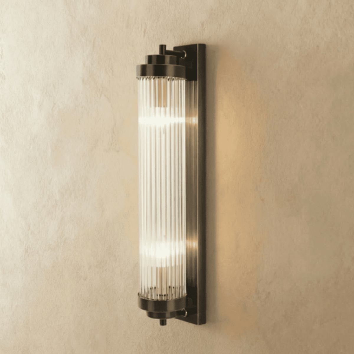Clérachic wall light in dark bronze-black with a ribbed glass rod cylinder and two lit bulbs, on limewash.