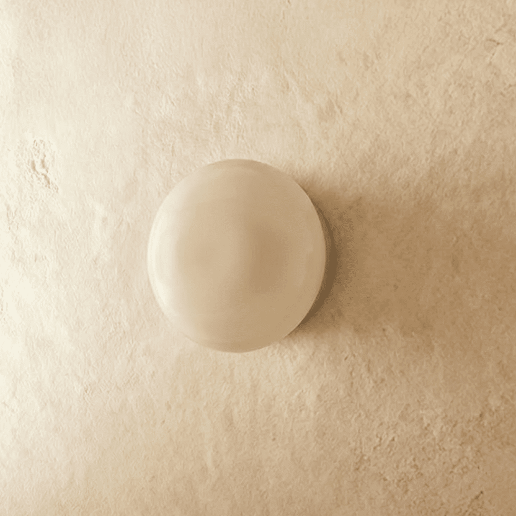 Clérachic round opal glass dome wall light, switched off, sitting flush on a limewashed plaster wall.
