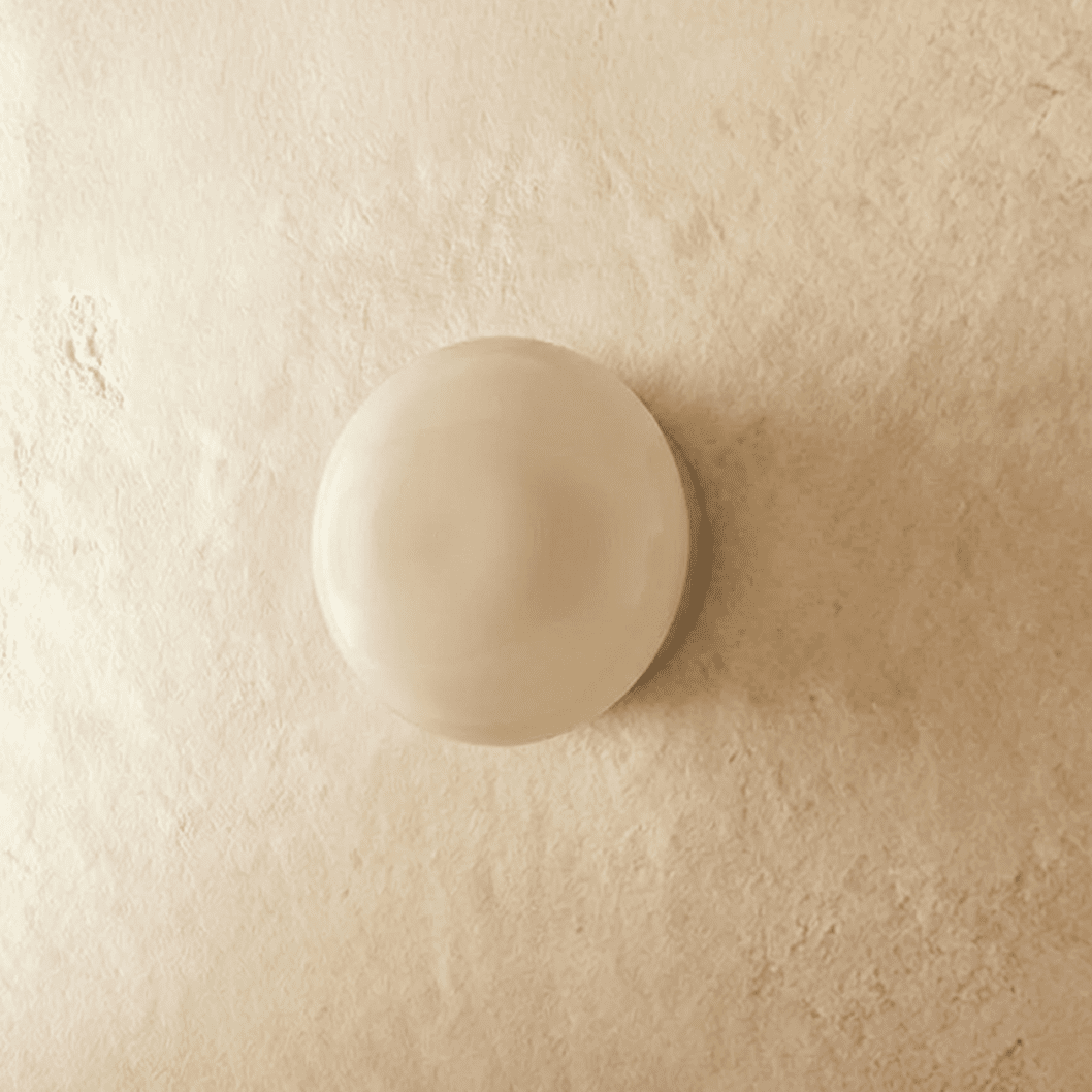 Clérachic round opal glass dome wall light, switched off, sitting flush on a limewashed plaster wall.