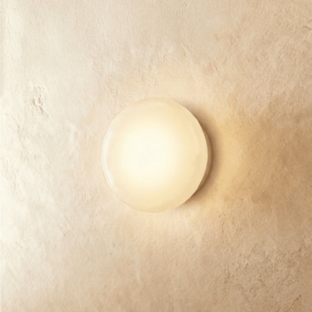 Clérachic round opal glass dome wall light glowing warm and soft, flush against a limewashed plaster wall.