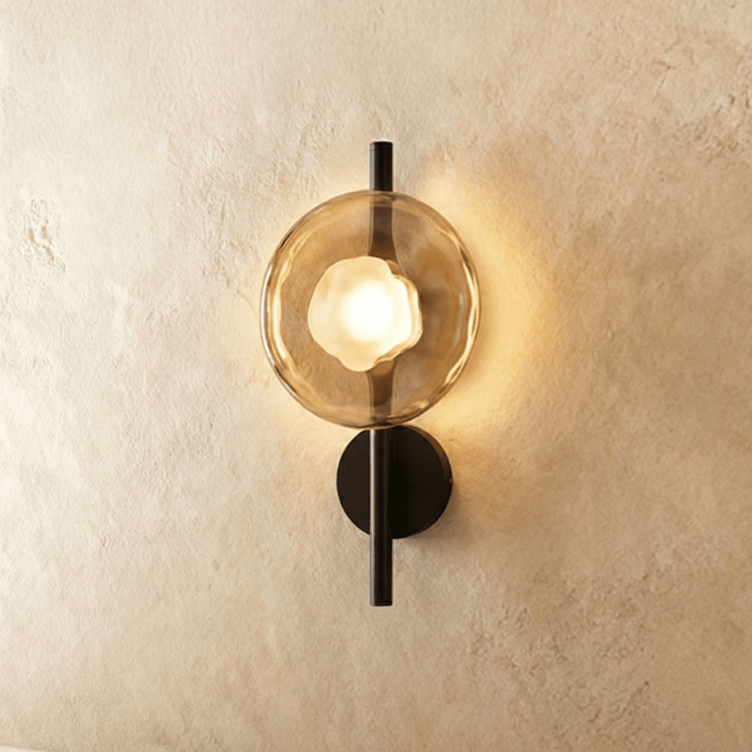 Clérachic wall light with a single amber glass disc and frosted bulb glowing on a slim black rod with a round backplate.