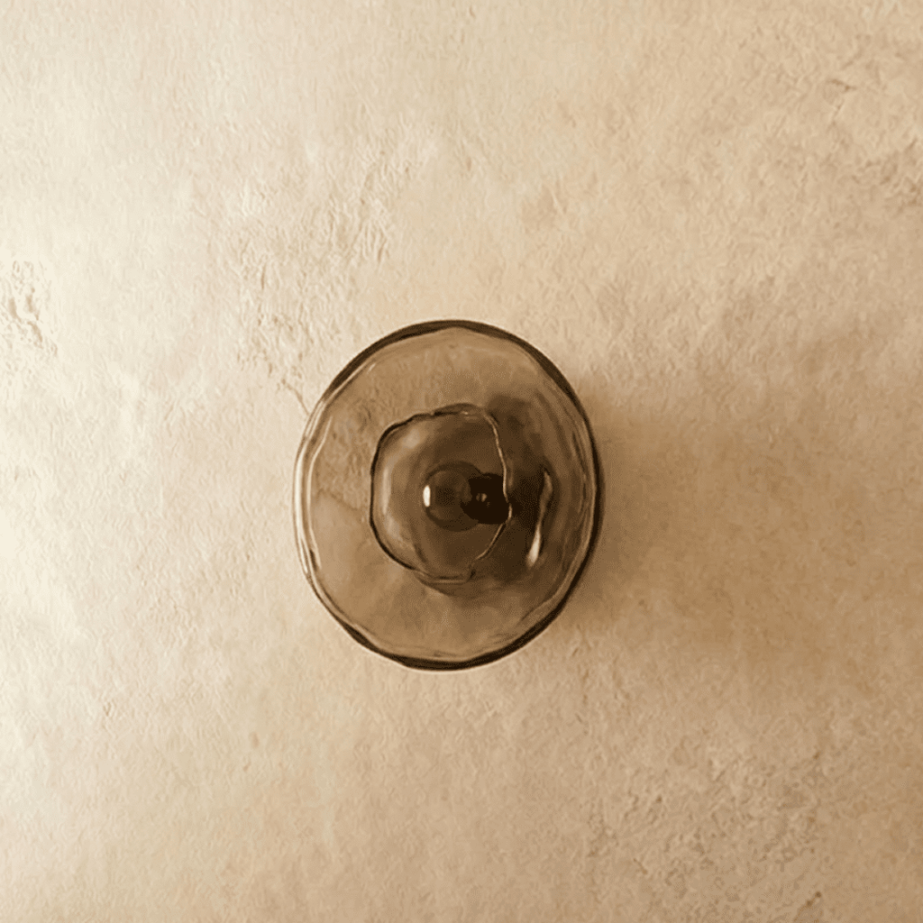 Clérachic flush round wall light with a smoky glass disc and dark bulb in the centre, switched off on a plaster wall.