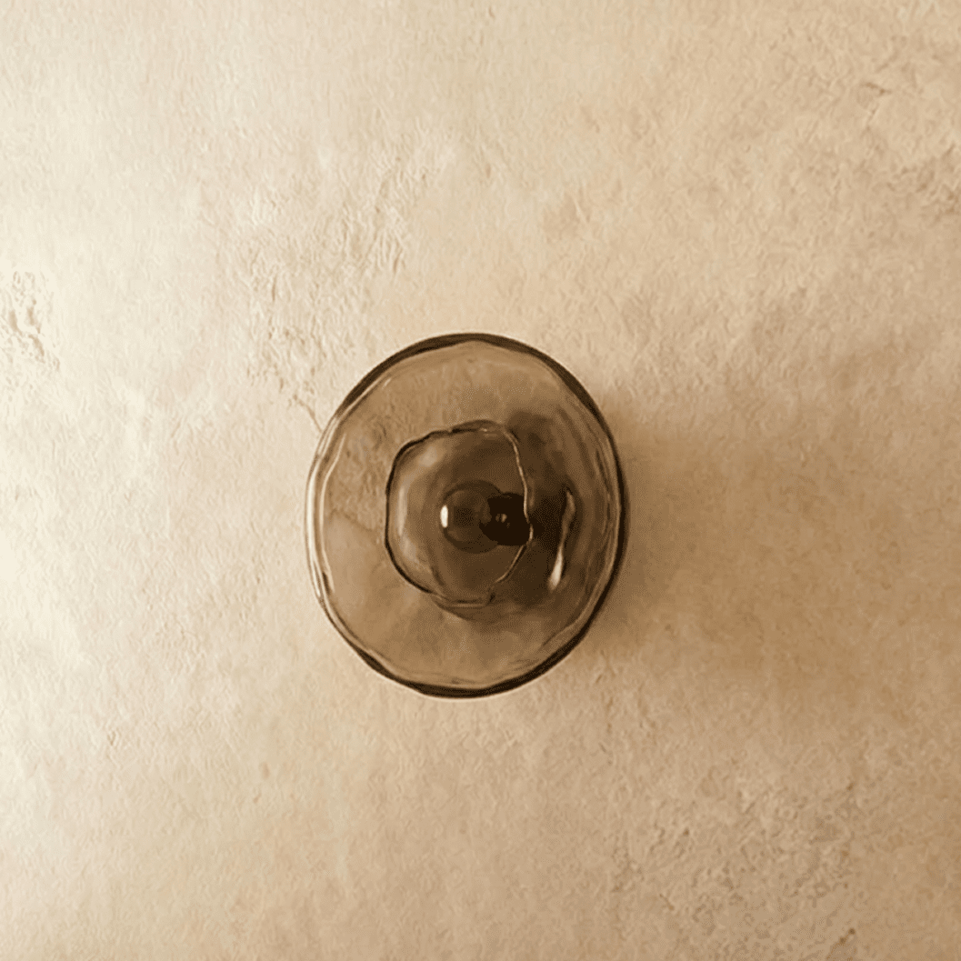 Clérachic flush round wall light with a smoky glass disc and dark bulb in the centre, switched off on a plaster wall.