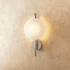 Clérachic wall light with a frosted white glass globe on a polished chrome rod and round backplate, glowing warm.