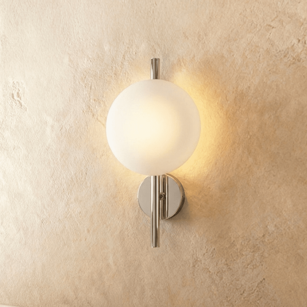 Clérachic wall light with a frosted white glass globe on a polished chrome rod and round backplate, glowing warm.
