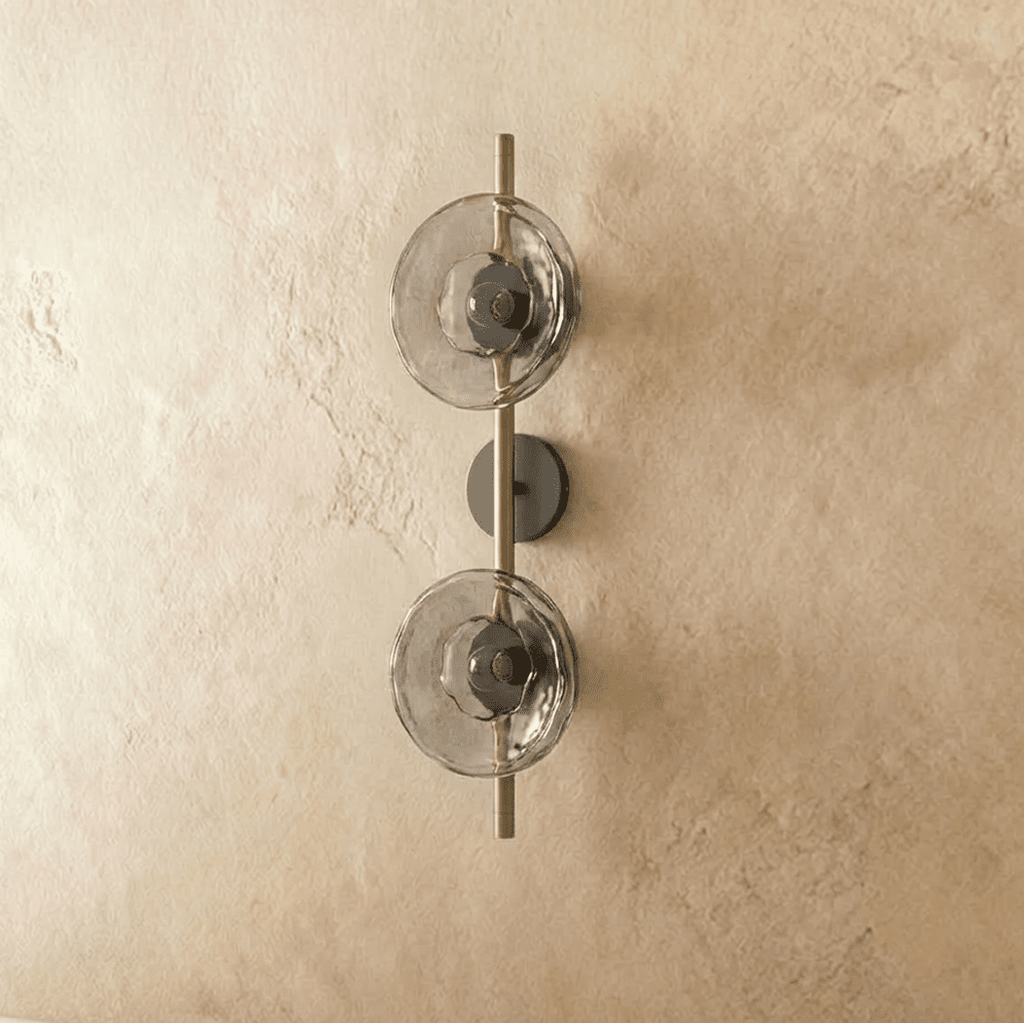 Clérachic two-shade wall light with smoky glass discs on a brushed brass rod and dark backplate, switched off.