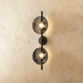 Clérachic two-shade wall light with smoky grey glass discs glowing warm on a slim black vertical rod and round backplate.