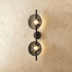 Clérachic two-shade wall light with smoky grey glass discs glowing warm on a slim black vertical rod and round backplate.