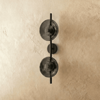Clérachic two-shade wall light with smoky grey glass discs on a black vertical rod and backplate, switched off.
